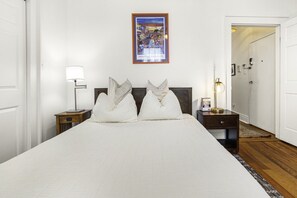 A hotel room with a large bed, two bedside tables, a nightstand, a framed picture on the wall, and a door leading to another room.