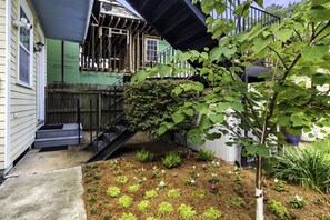 A residential property with a wooden deck, a small garden with various plants, and a staircase leading to a covered area. - Creole Cottage, Designer, Balcony (New Orleans)