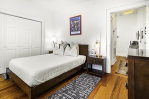 A bedroom with a bed, bedside tables, a lamp, a rug, and a door leading to another room.