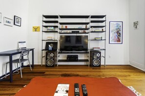 A living room with a TV, speakers, and a coffee table with remote controls. - Creole Cottage, Designer, Balcony (New Orleans)