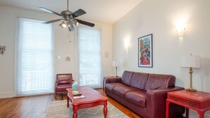A living room with a red leather sofa, a wooden coffee table, a red side table, a ceiling fan, and a painting on the wall. - Creole Cottage, Designer, Balcony (New Orleans)