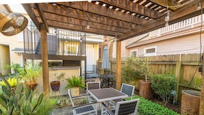 A patio with a table and chairs, surrounded by potted plants and a wooden fence. - Creole Cottage, Designer, Balcony (New Orleans)