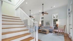 A spacious living area with a wooden staircase, a ceiling fan, and a comfortable seating arrangement. - Gulf Views from Tower in Seaside, 6 Houses to Private Beach & 2 Adult Bikes! (Santa Rosa Beach)
