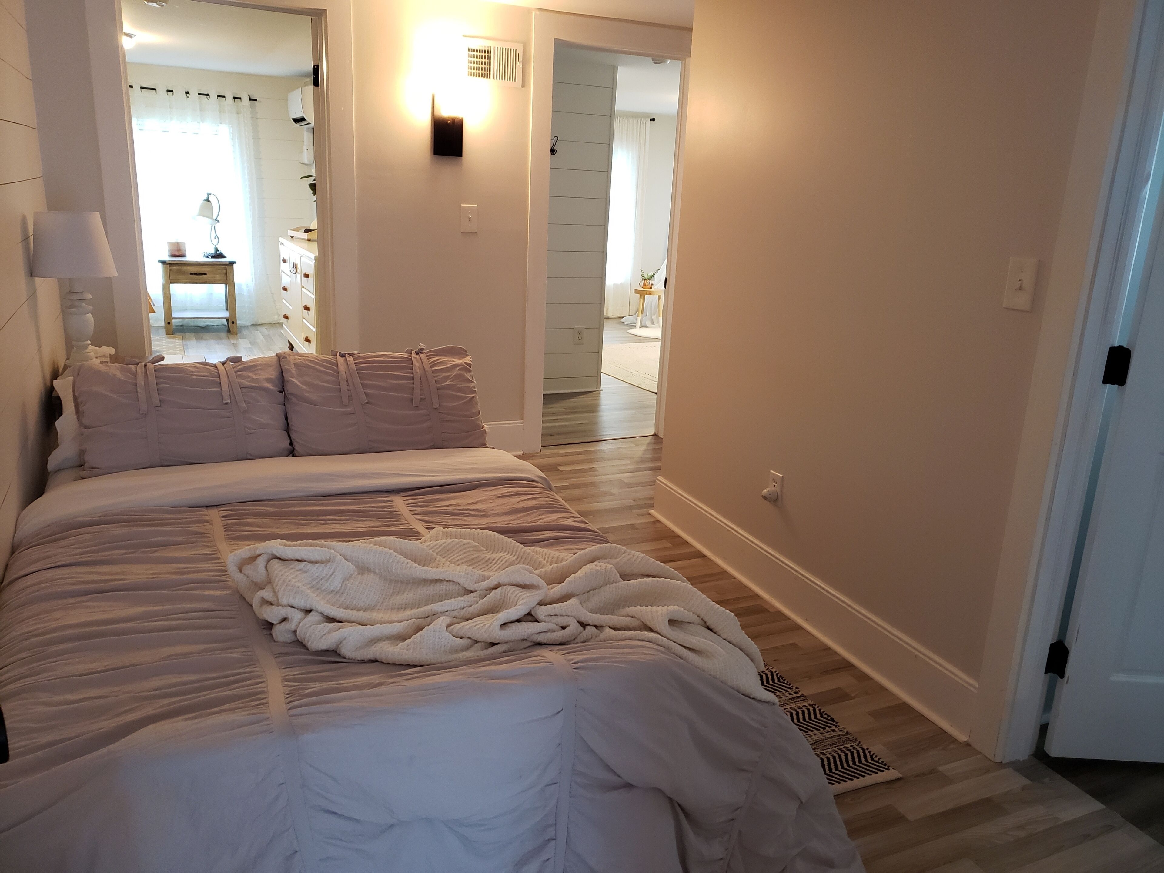 A bedroom with a bed, bedside table, lamp, and a view of a hallway leading to a bathroom.