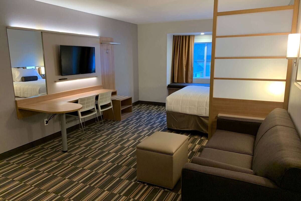 A hotel room with a bed, a desk, a chair, a TV, and a window with curtains.
