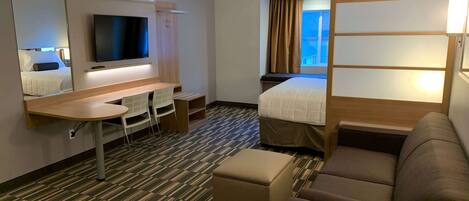 A hotel room with a bed, a desk, a chair, a TV, and a window with curtains.