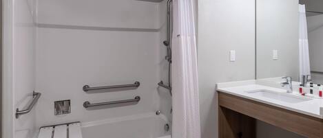 Une salle de bain équipée d’une douche, de barres d’appui, d’un lavabo et d’un miroir.