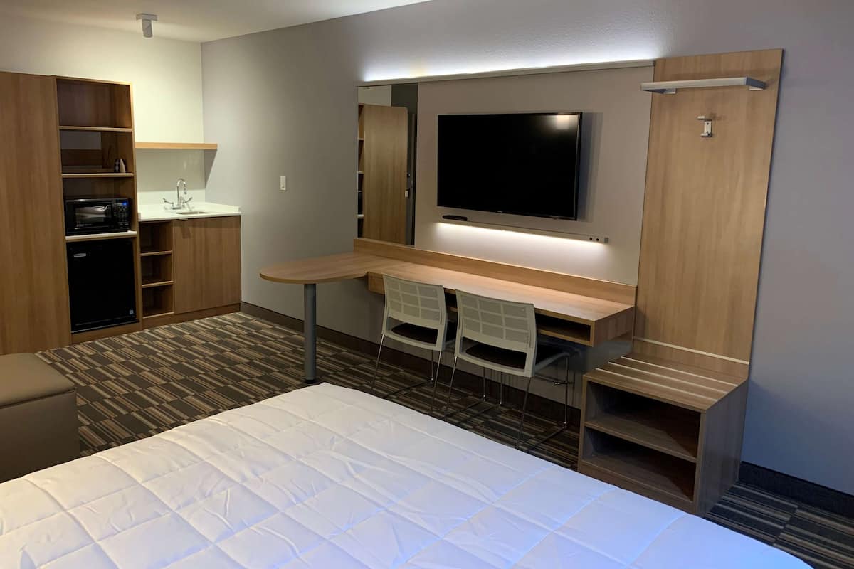 A hotel room with a bed, a desk with two chairs, a TV, a microwave, and a wardrobe.