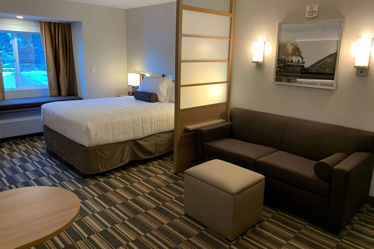 A hotel room with a bed, a sofa, a small table, and a window with curtains.