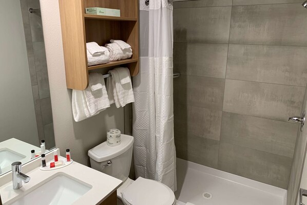 Une salle de bain moderne équipée d’une douche, de toilettes et d’un lavabo. Des serviettes et des articles de toilette sont disposés sur les étagères.