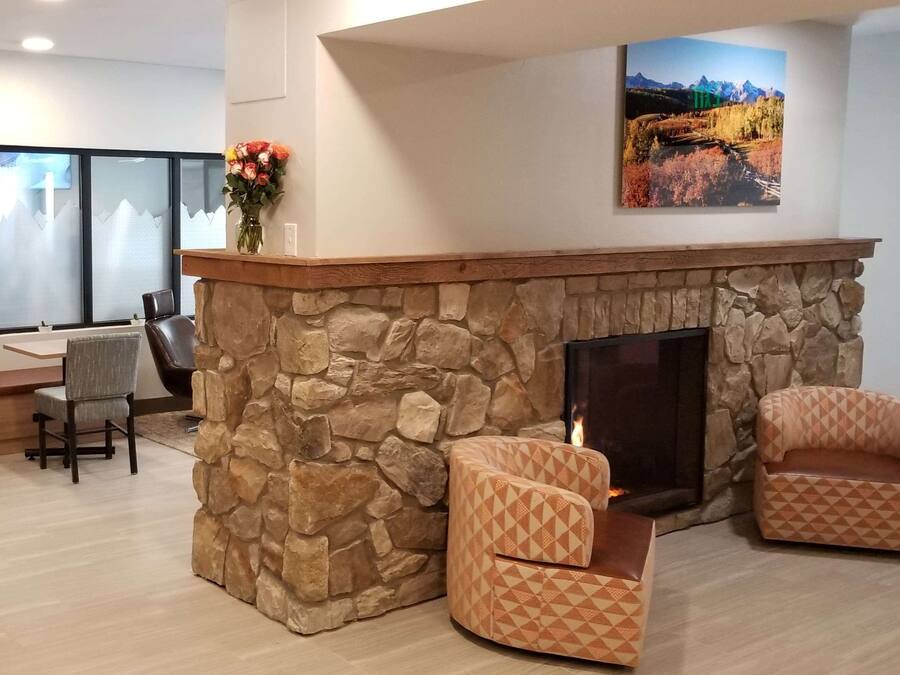 Een woonkamer met een stenen openhaard, twee gestreept fauteuils, een eethoek met een bank en een groot raam.