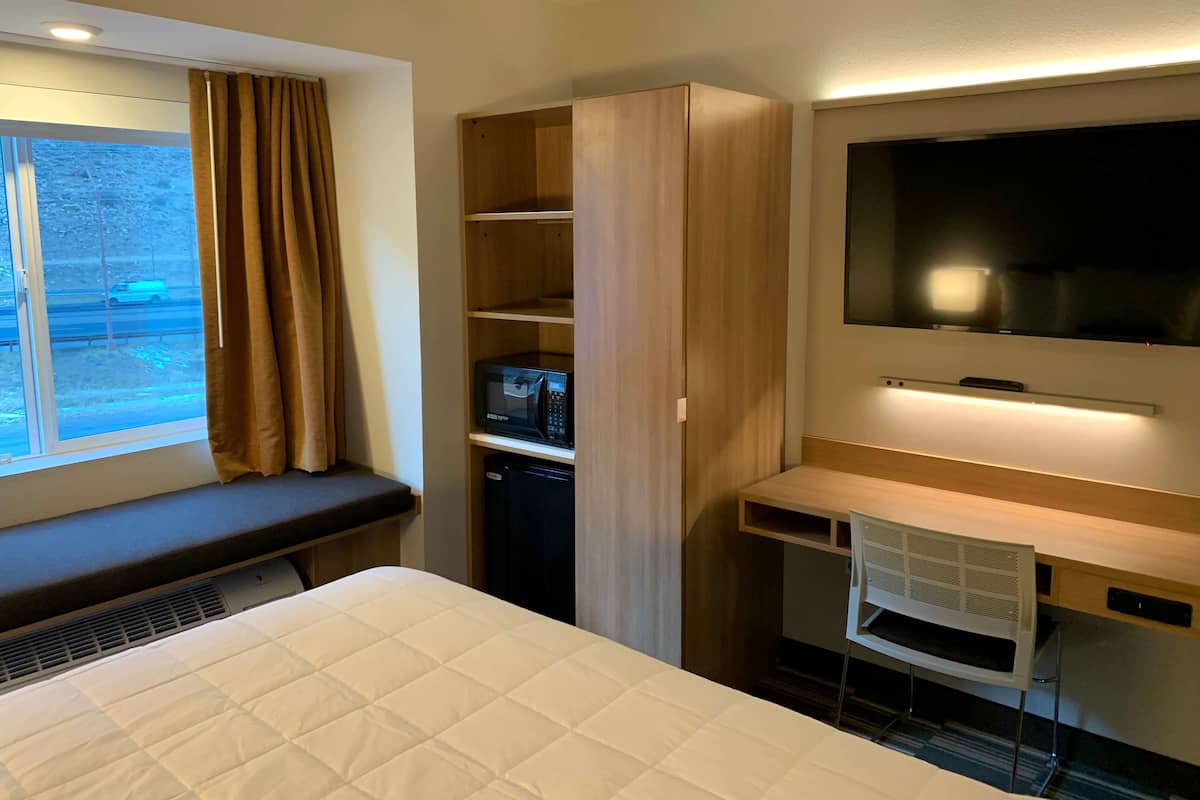 A hotel room with a bed, a desk, a TV, a microwave, and a window with curtains.