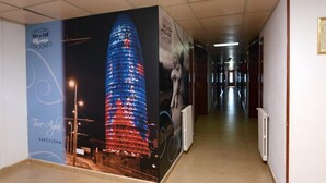 A corridor with a large poster of a building, a radiator, and a wall with a sign. - Don Angel Hotel (Santa Susanna)