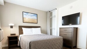 Una habitación de hotel con cama, mesita de noche, televisión, cómoda y un cuadro en la pared.