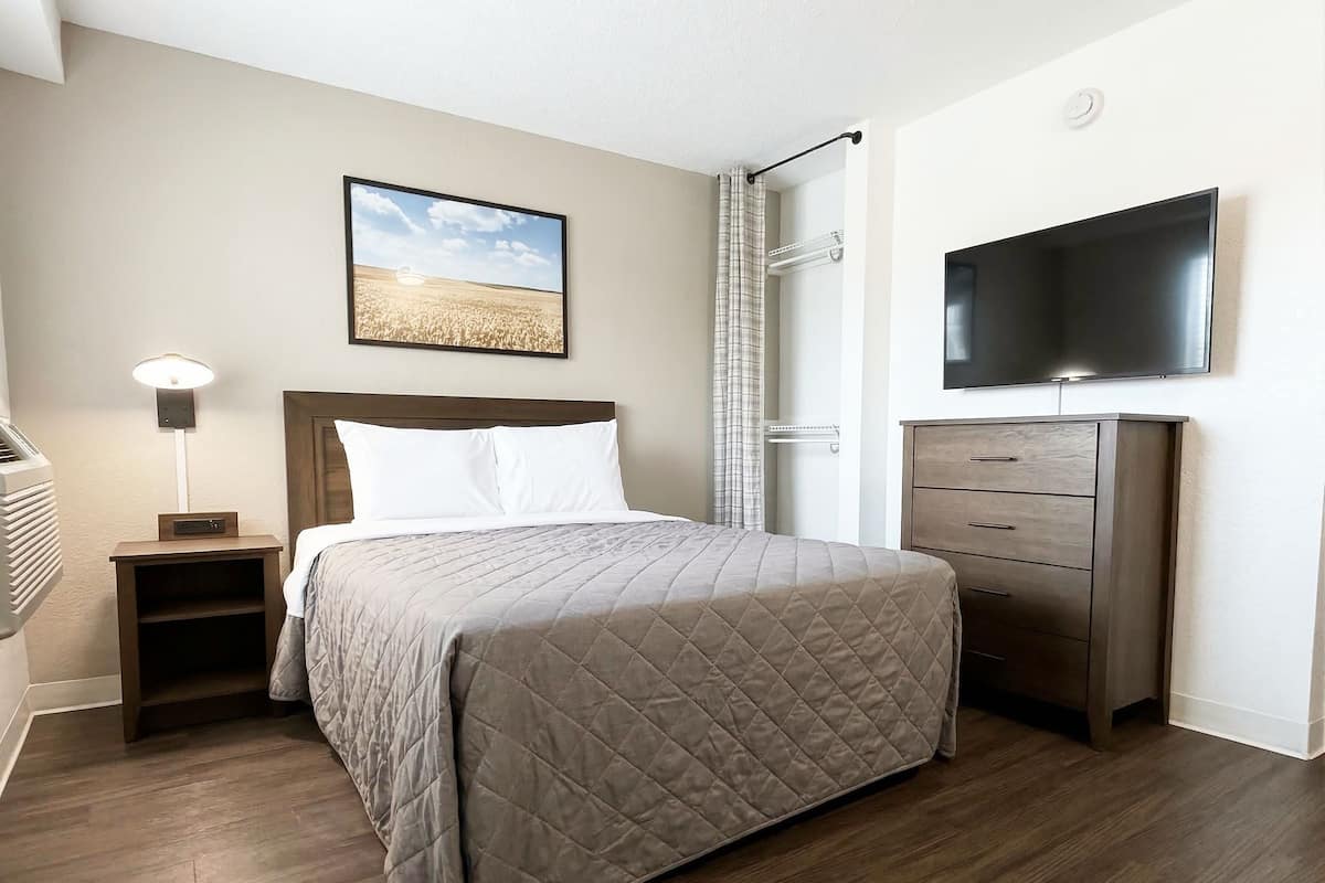 Una habitación de hotel con cama, mesita de noche, televisión, cómoda y un cuadro en la pared.