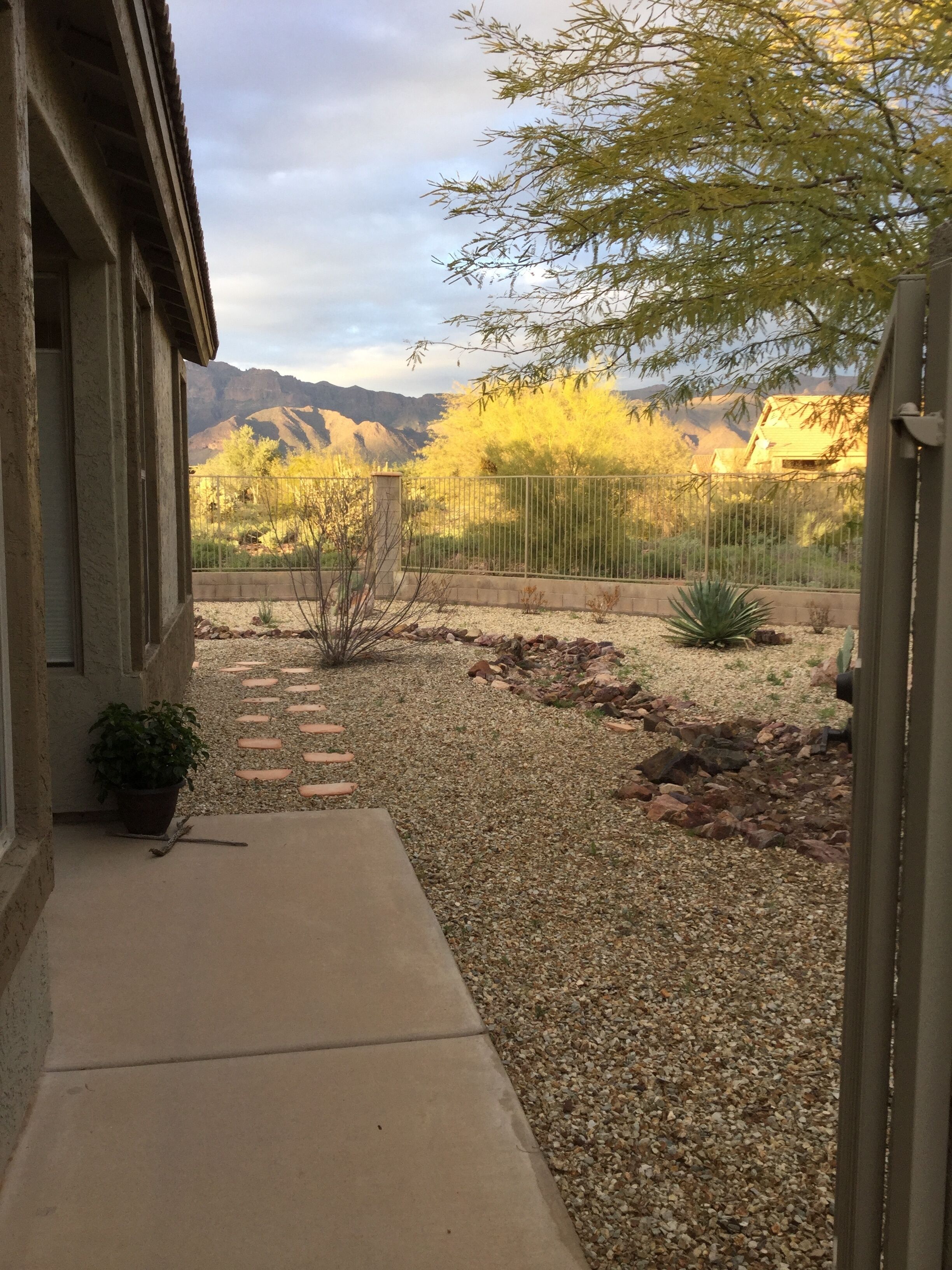 A patio area with a gravel path, a potted plant, and a view of mountains in the background.