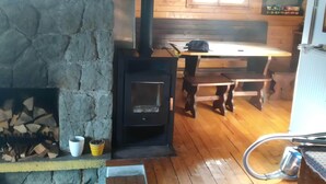 A rustic cabin interior with a stone fireplace, wooden flooring, and a wooden dining table. - Villa in Nature (Mozirje)