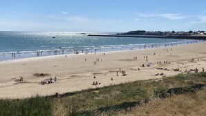 A wide beach with people walking and sunbathing, a rocky breakwater, and buildings in the background. - Waterfront apartment in St Gilles Croix de Vie (Saint-Gilles-Croix-de-Vie)