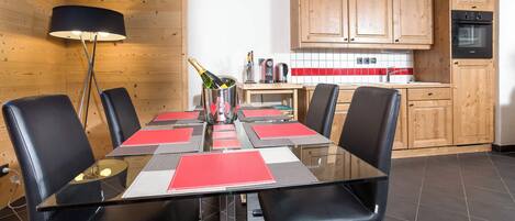 A modern dining area with a glass table, black chairs, and a wooden wall.