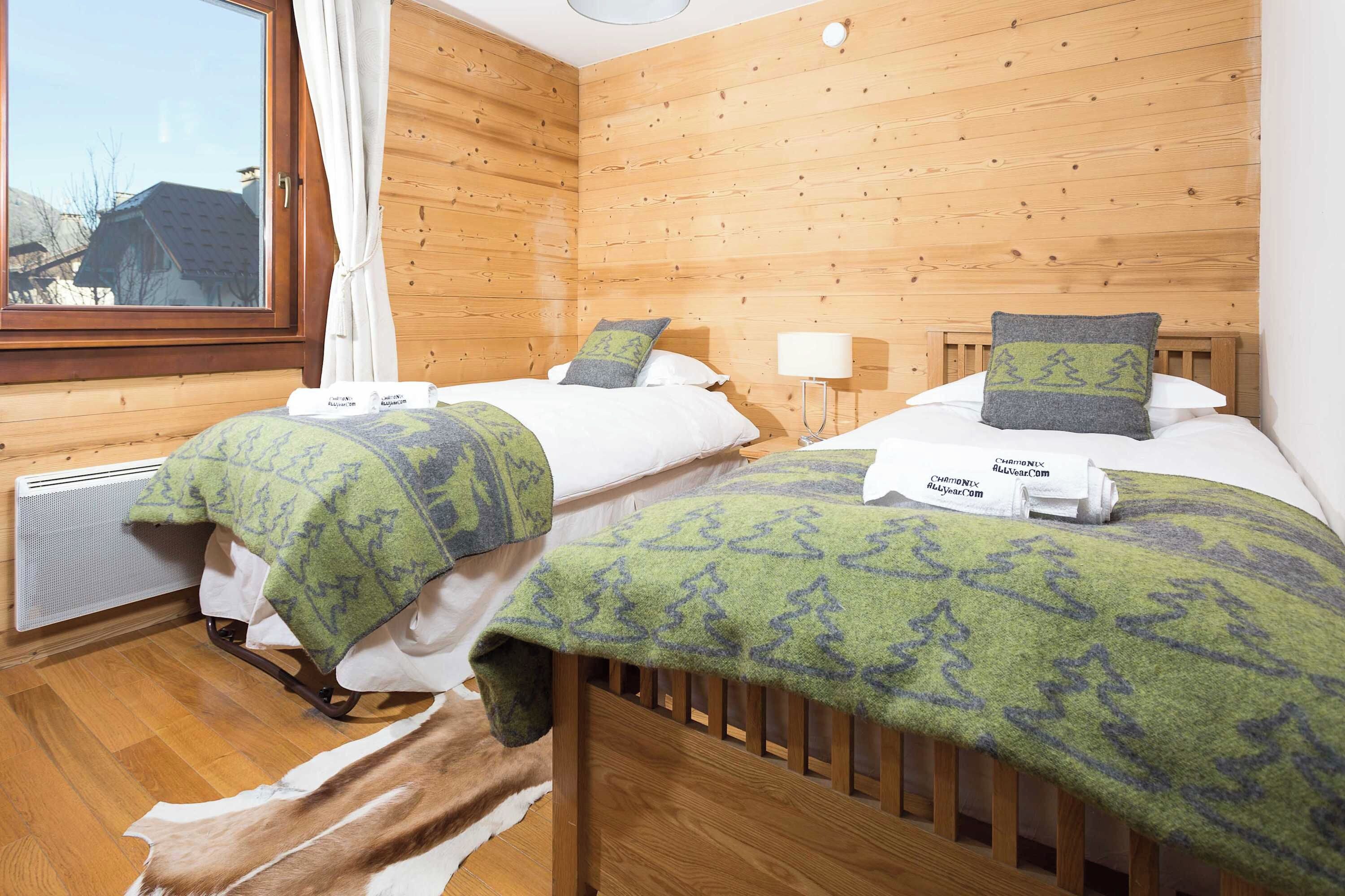 A room with two beds, wooden walls, a window, and a radiator.