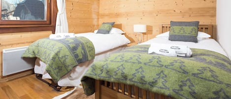 A room with two beds, wooden walls, a window, and a radiator.