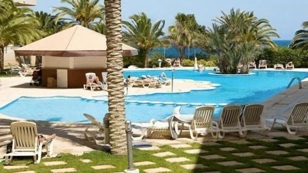 A pool area with lounge chairs and a small building, surrounded by palm trees. - Riviera Beach Apartments (Pilar de la Horadada)