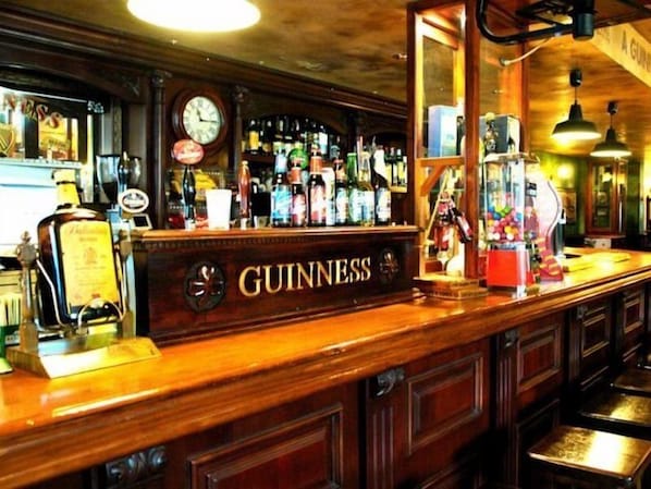 A bar with a Guinness sign, a clock, and various bottles. - Riviera Beach Apartments (Pilar de la Horadada)