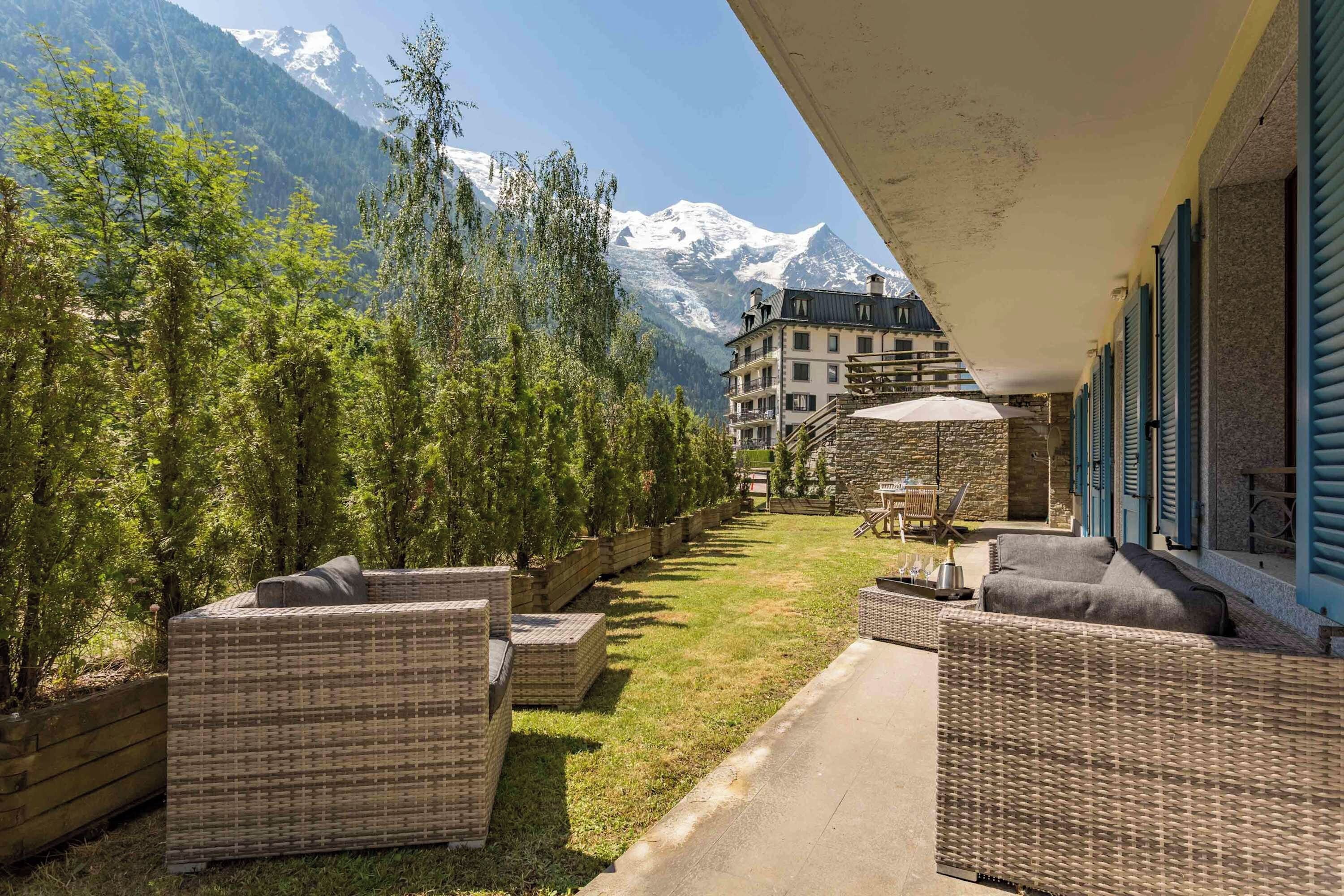 A hotel balcony with wicker furniture, a stone wall, and a mountain view.