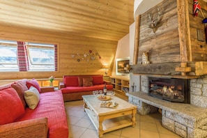 L’intérieur chaleureux d’un chalet avec un plafond en bois, une cheminée, un canapé et une table à manger.