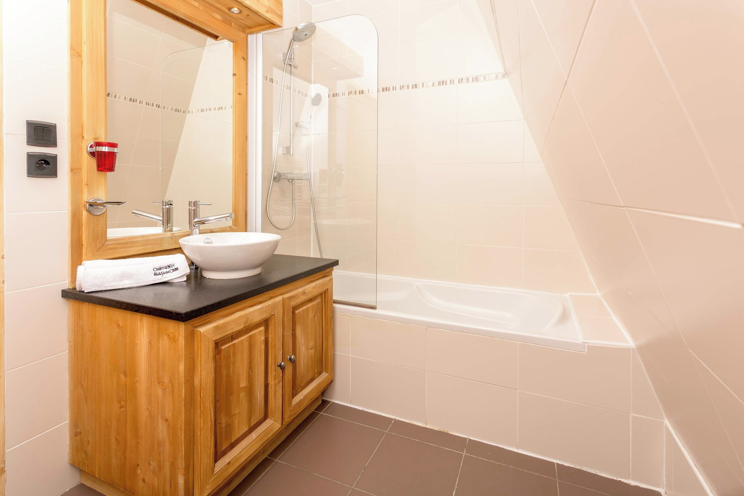 Ein Badezimmer mit einem Holzkosmetikschrank, einem weißen Waschbecken, einem Spiegel, einer Glasdusche und einer Badewanne.