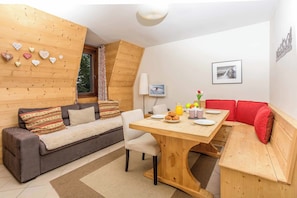 Une pièce chaleureuse avec un plafond en bois, un canapé, une table à manger où sont disposés des aliments pour le petit-déjeuner et un banc rouge.