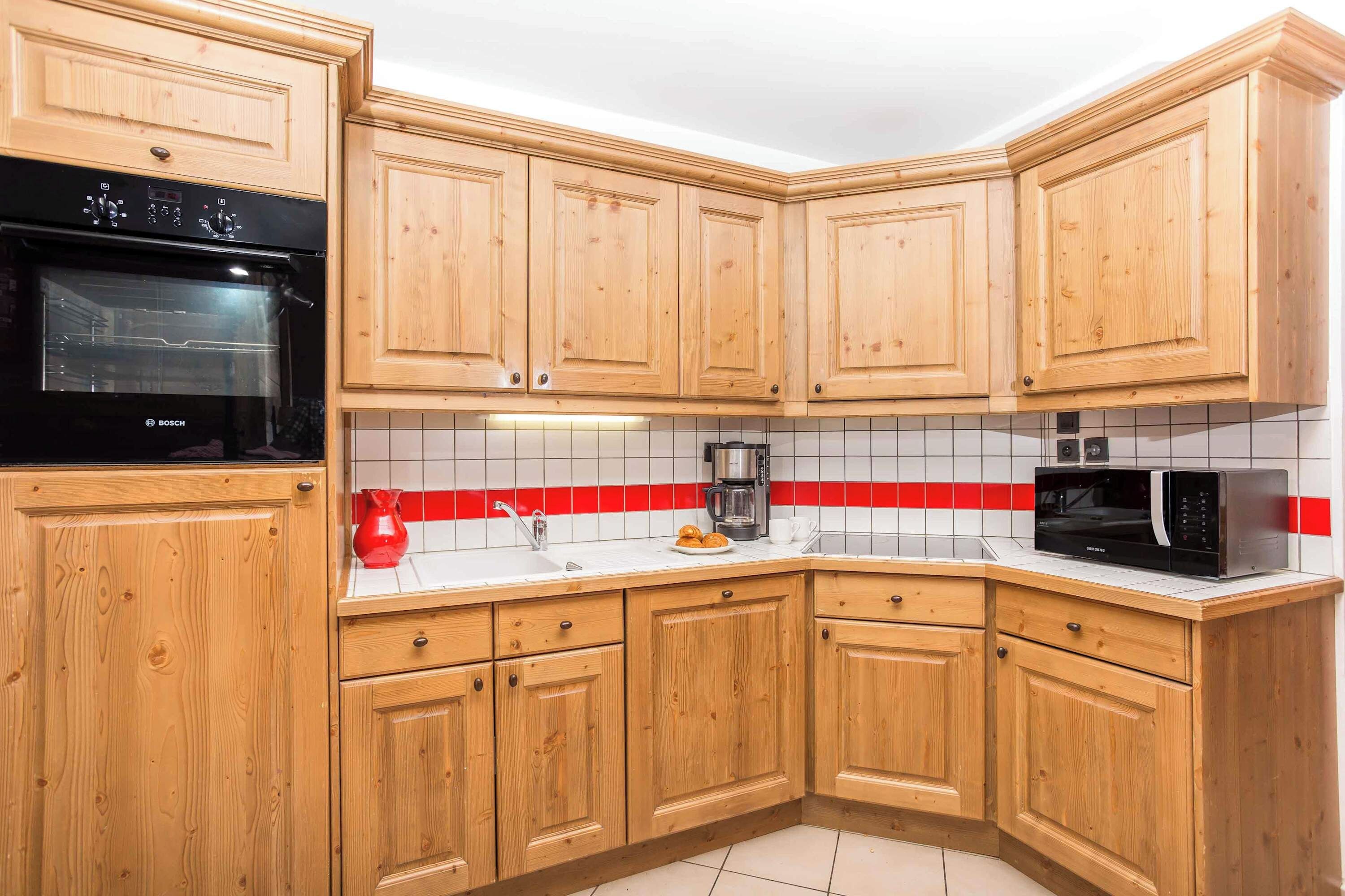 Cozinha com armários de madeira, forno Bosch, micro-ondas Samsung e painel de azulejos vermelho e branco.