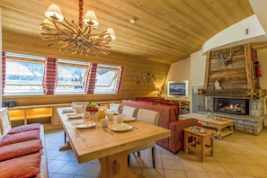 A spacious room with a wooden ceiling, a fireplace, a television, and a dining area with a table set for four. - Ski at Le Paradis 18 & 18b apt, Chamonix All Year (Chamonix)