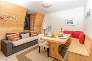 A cozy room with a wooden ceiling, a sofa, a dining table with breakfast items, and a red bench.