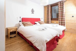 A double bed with red headboard and white bedding, a small wooden nightstand, and a window with patterned curtains. - Ski at Le Paradis 18 & 18b apt, Chamonix All Year (Chamonix)