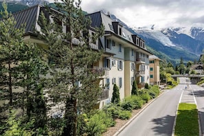 Un edificio de varios pisos con balcones, rodeado de vegetación y montañas al fondo.