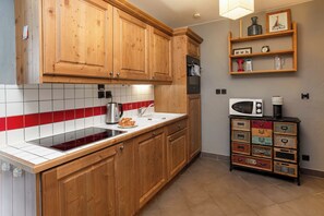 Una cocina con armarios de madera, un salpicadero con baldosas rojas y blancas, un hervidor de acero inoxidable, un microondas y un aparador de estilo vintage.