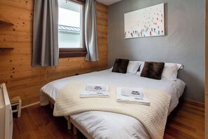 Un dormitorio con una cama, dos almohadas, una ventana con cortinas, un cuadro en la pared y un radiador.