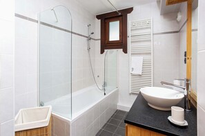 A modern bathroom with a glass-enclosed shower, a freestanding bathtub, a white sink with a black countertop, and a wooden cabinet above the mirror.