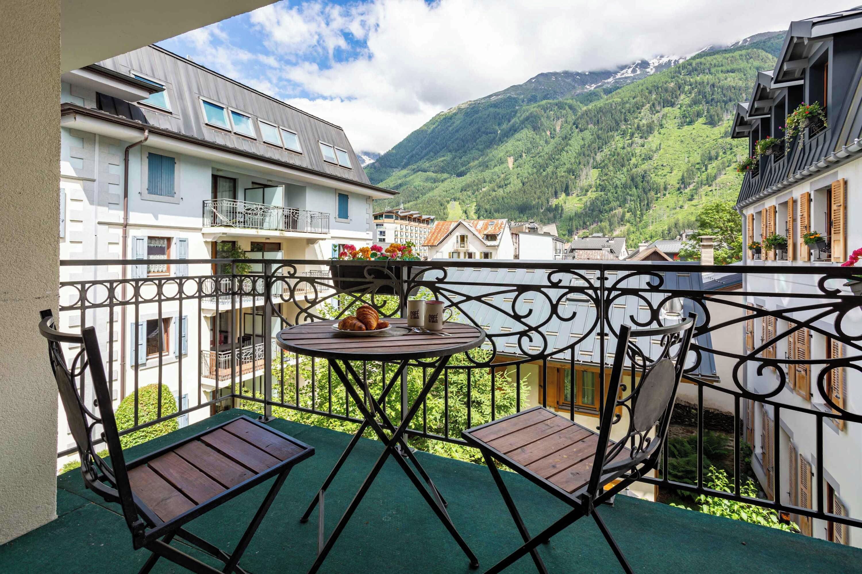 Ein Balkon mit Tisch und Stühlen mit Blick auf eine gebirgige Landschaft.