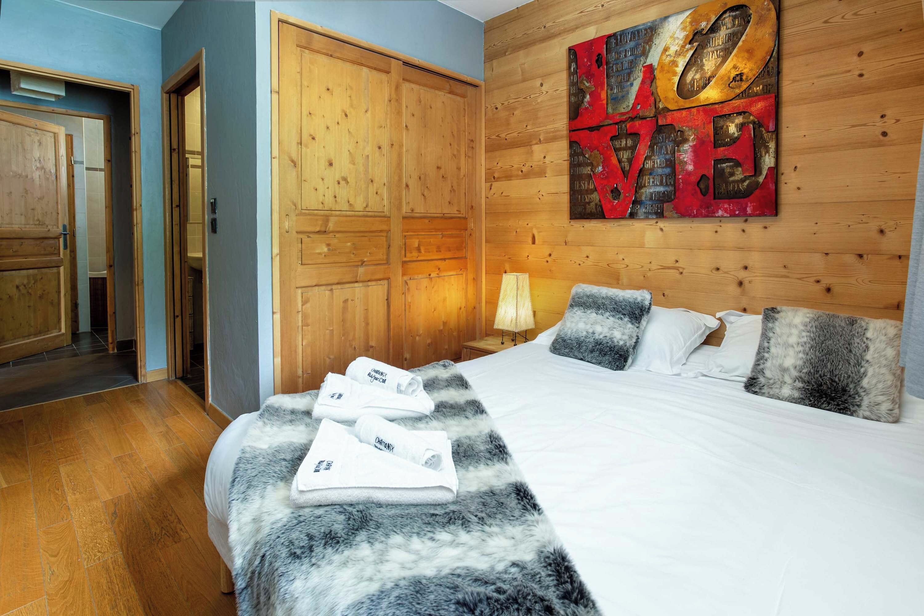 Een hotelkamer met een houten garderobe, een bed met wit beddengoed, en een groot abstract kunstwerk aan de muur.