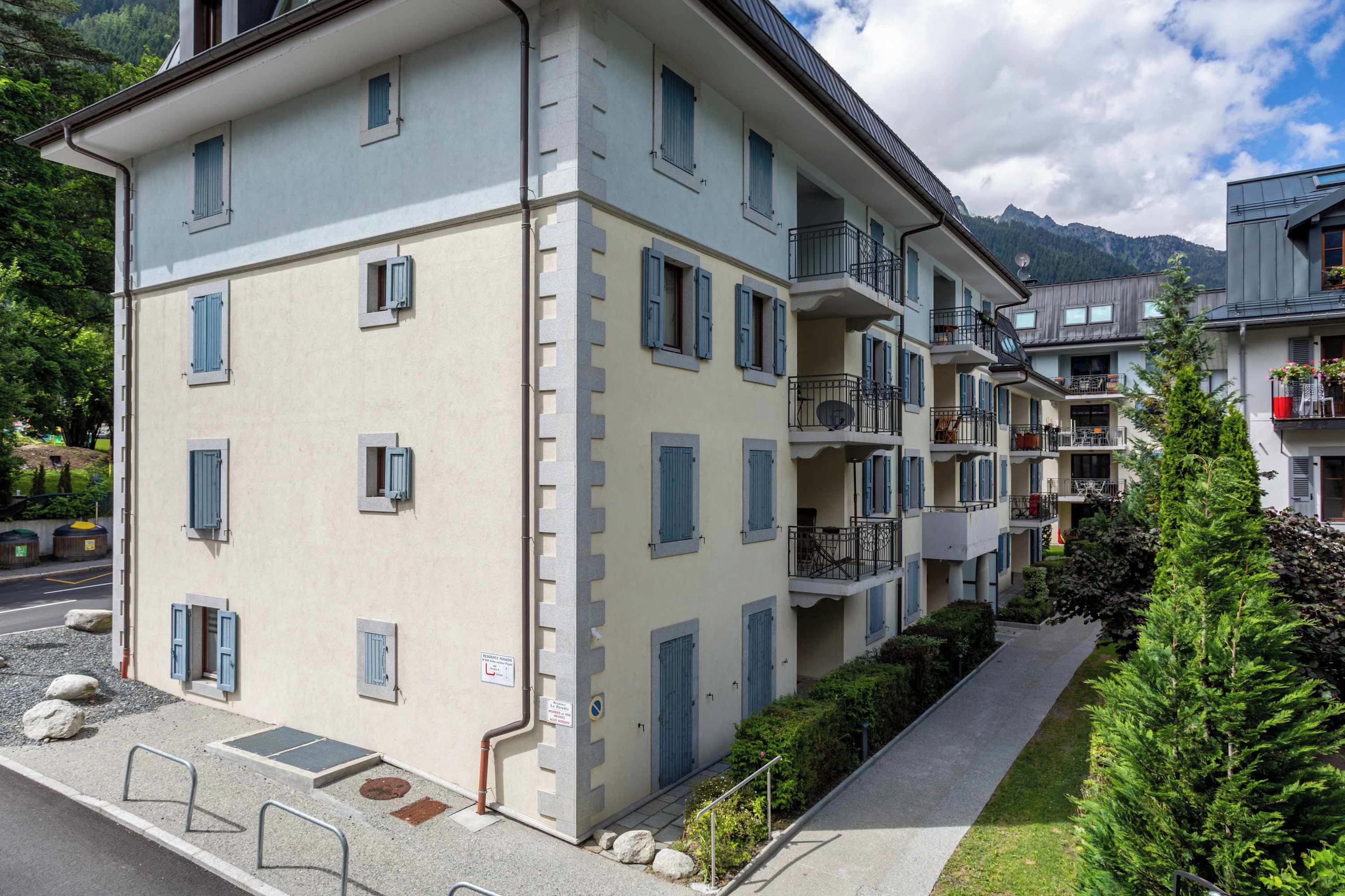 A multi-story building with balconies, a paved pathway, and a mountain backdrop.