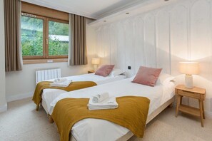 Une chambre d’hôtel avec deux lits, une fenêtre avec des rideaux, un radiateur et une table de chevet avec une lampe.
