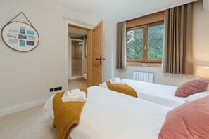 A hotel room with two beds, a window with curtains, a door leading to a bathroom, and a wall-mounted photo collage.