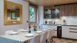 Zona pranzo con tavolo apparecchiato per sei, cucina dotata di elettrodomestici moderni e un ampio specchio a parete.