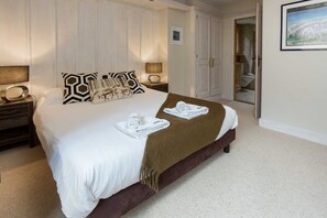 A neatly made bed with white linens and a brown throw blanket, two bedside tables with lamps, a framed picture on the wall, and a door leading to a bathroom. - Chamois Apartment, amazing views Chamonix All Year (Chamonix)