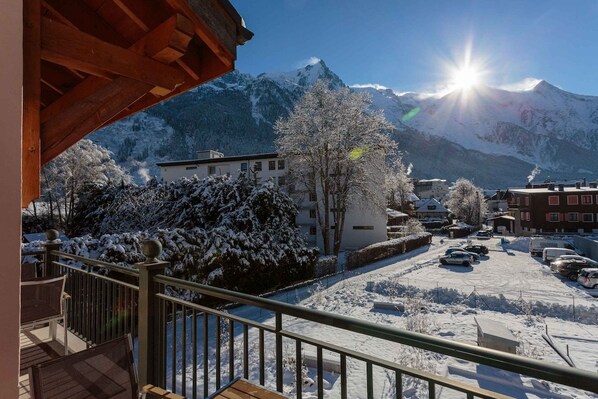 A snowy mountain landscape with a clear sky, a balcony with outdoor seating, and a parking area.