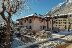 A traditional chalet-style building with a snow-covered roof, situated in a mountainous area with a clear sky.