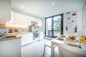 A modern kitchen with white cabinetry, a built-in oven, and a dining area with a table set for breakfast. - Rupicapra apartment, Skiing, Chamonix All Year (Chamonix)