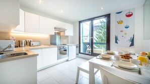 A modern kitchen with white cabinetry, a built-in oven, and a large window with a view of greenery. - Rupicapra apartment -  an apartment that sleeps 6 guests  in 3 bedrooms (Chamonix)